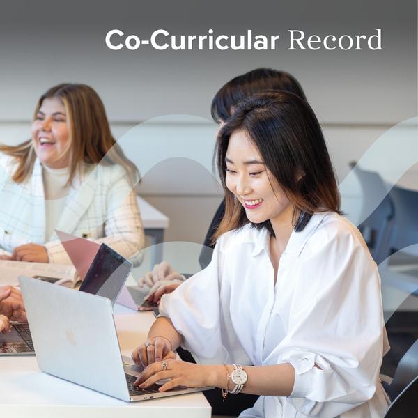 A student looking at a laptop, while others are talking in the background.