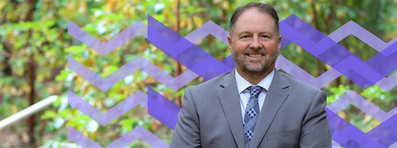 Dennis Johnson with the VIU ripples background and trees behind him